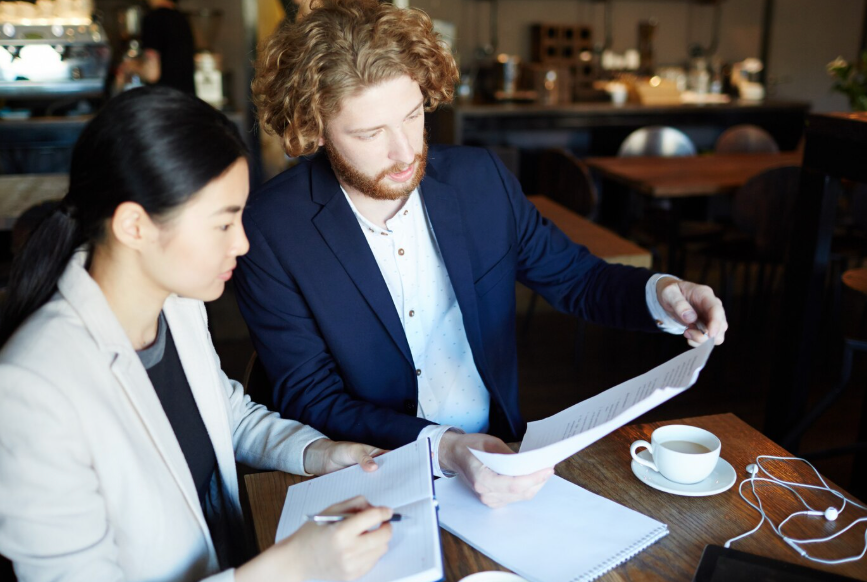Two professionals reviewing documents together during business meeting in café workspace.